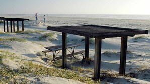 A beach with wooden structures, including benches and tables, and two people walking.