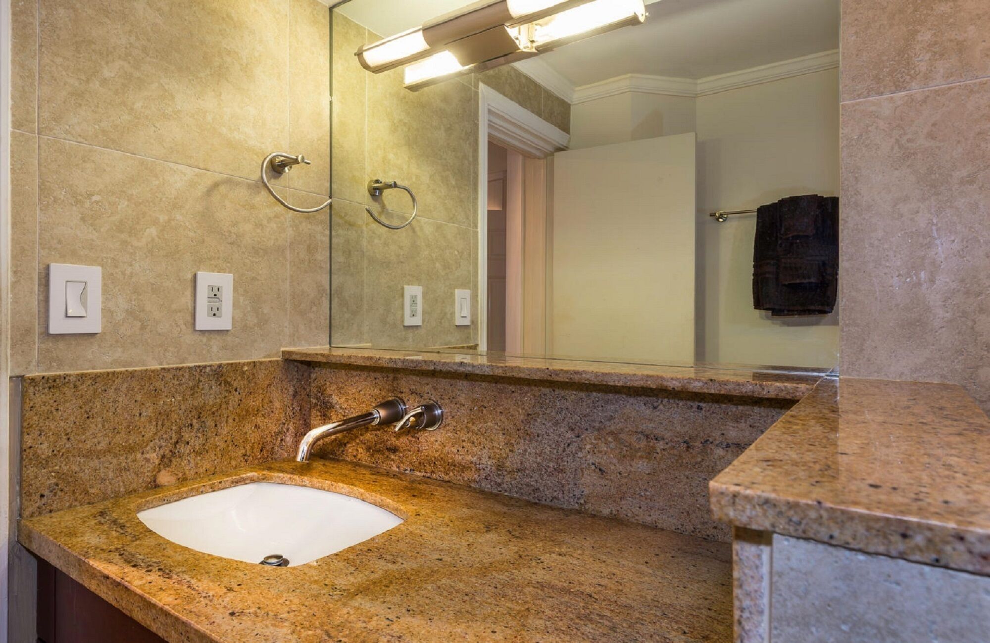 Un baño con lavamanos de encimera de granito, un espejo y un perchero para toallas.