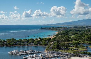 A marina with numerous boats docked, a beach with palm trees, and a cityscape in the background. - Absolutely Ocean View - Great Location - Free Parking-Sleeps three (honolulu)