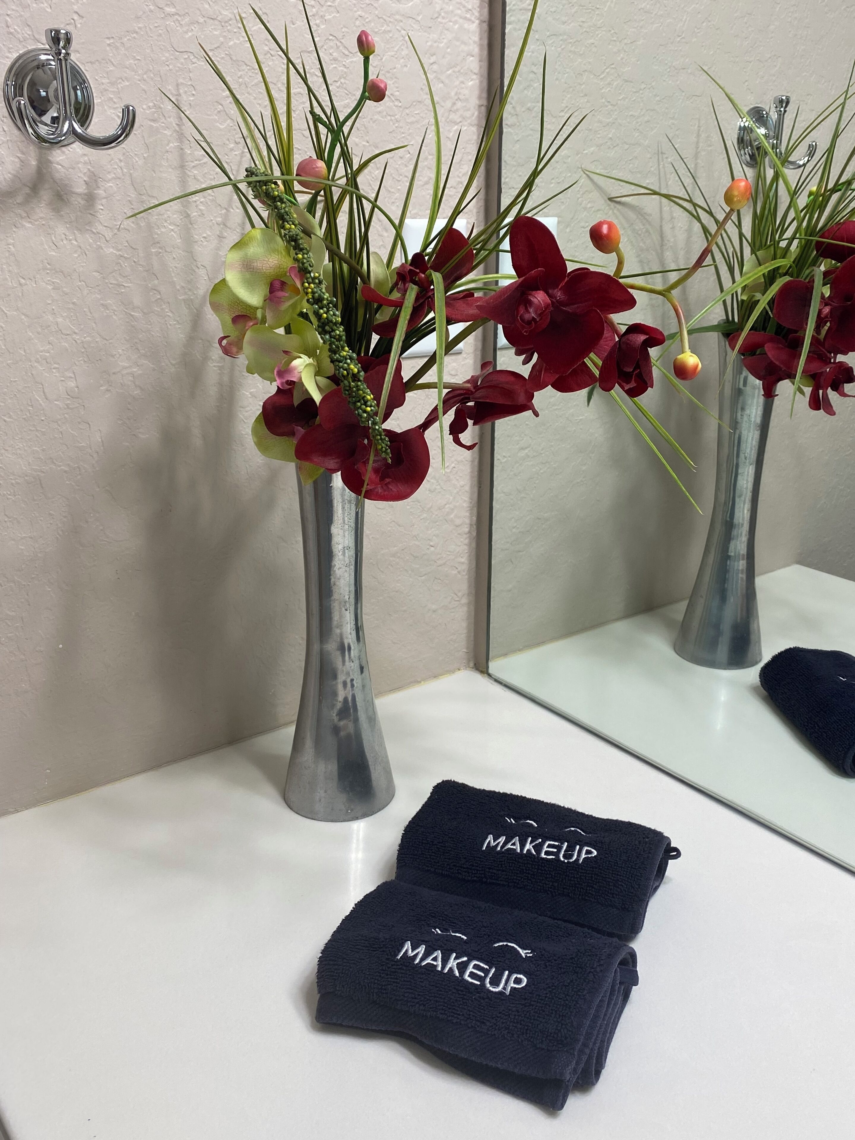 Un bany amb un mirall, un rentapeus i dos vas amb flors. Hi ha tovalloles amb la paraula "MAKEUP".
