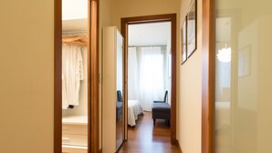 A hallway with wooden flooring leading to a bedroom with a bed and a chair. - A gem in the heart of the city (Padova)