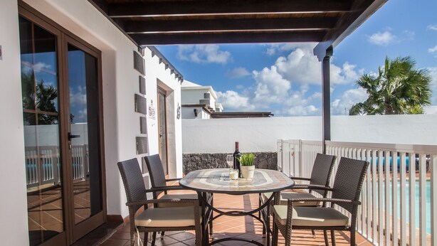 A patio with a round table and four chairs, a bottle of wine, and a small plant.