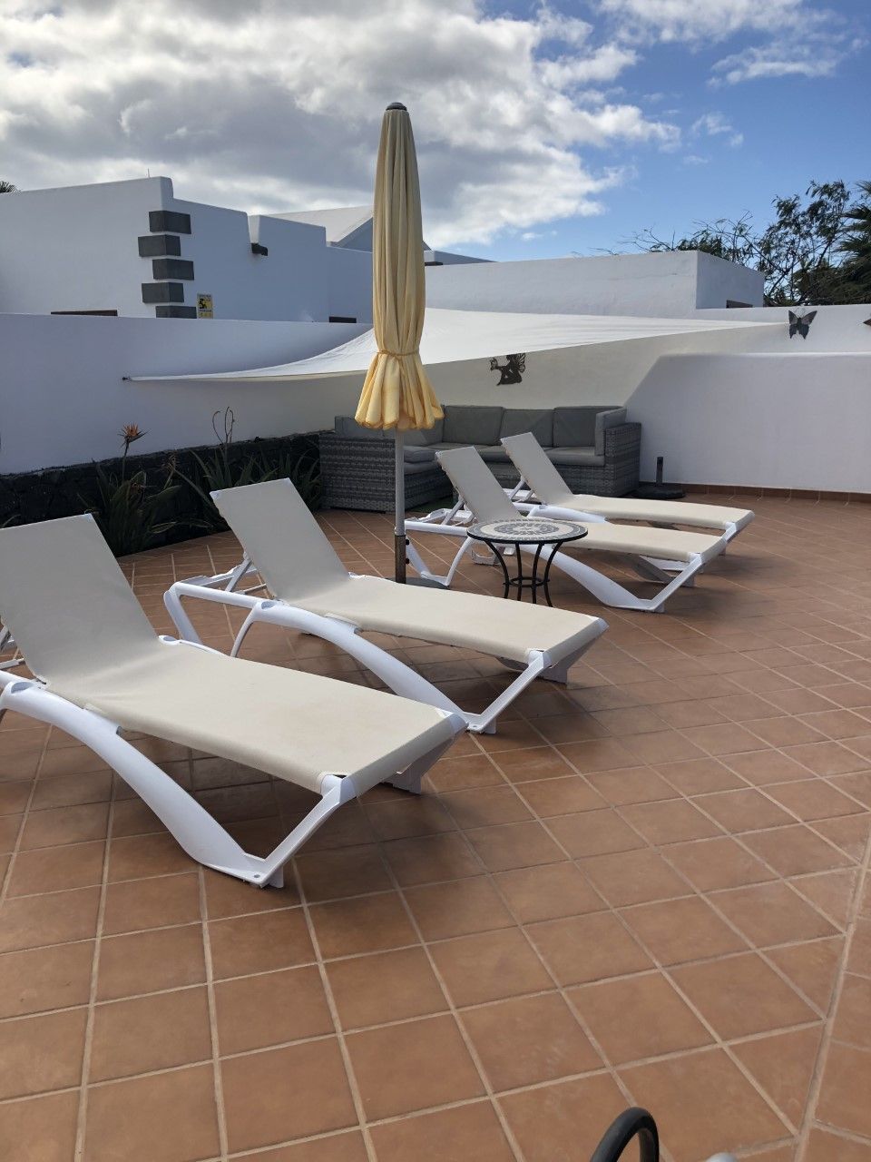 Een terras op het dak met witte lounge stoelen en een gele parasol, met een modern wit gebouw op de achtergrond.
