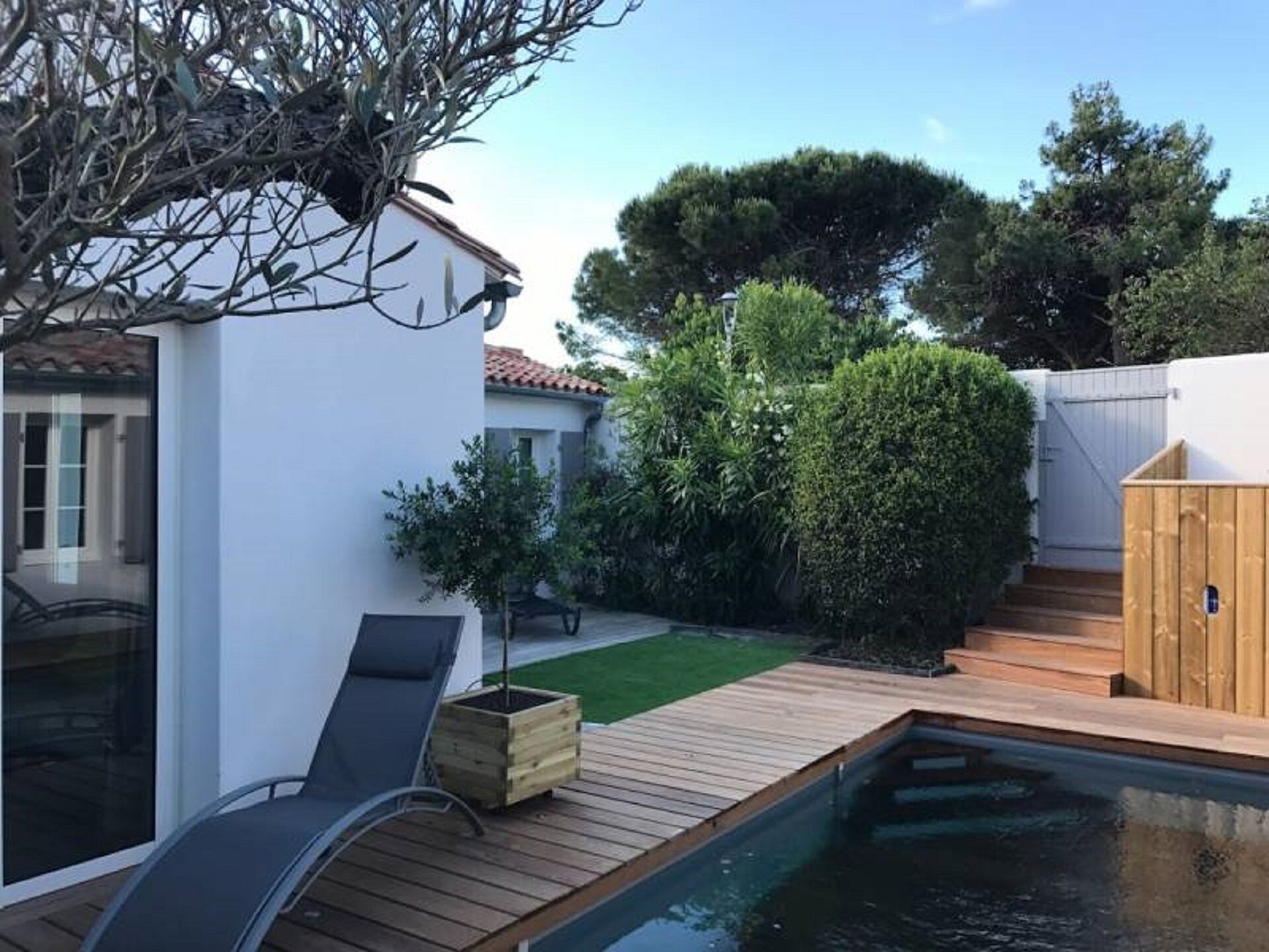 Ein Garten mit Schwimmbad, Holzterrasse und einem kleinen weißen Gebäude.