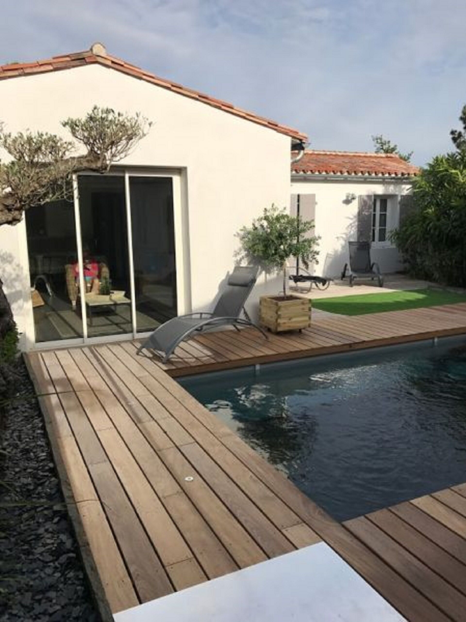 A modern house with a swimming pool, wooden deck, and a sliding glass door leading to a patio area.