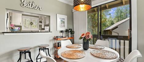 Een eetgedeelte met een ronde tafel, witte stoelen, een hanglamp en uitzicht op de omgeving.