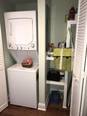 Une petite buanderie équipée d’un lave-linge à chargement frontal, d’un four à micro-ondes et d’une petite étagère contenant des produits de nettoyage.
