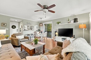 A living room with a ceiling fan, a television, and a dining area with a white table and chairs.