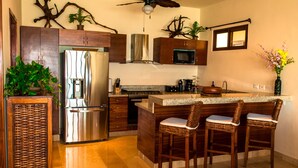 A modern kitchen with a central island, bar stools, stainless steel appliances, and decorative plants.