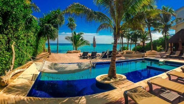 A pool area with lounge chairs, a hammock, and a view of the ocean.