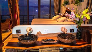 A bedroom with a large bed, a view of the ocean, and a wooden table with decorative bowls.