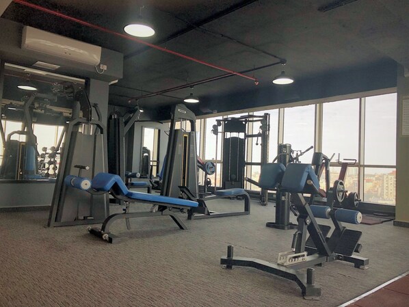 A gym with various exercise equipment, large windows, and a carpeted floor. - Carmel Hotel (Ramallah)