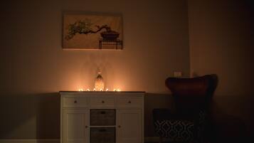 Una stanza scarsamente illuminata con un armadio bianco, una candela accesa, una sedia decorata e un quadro appeso al muro.