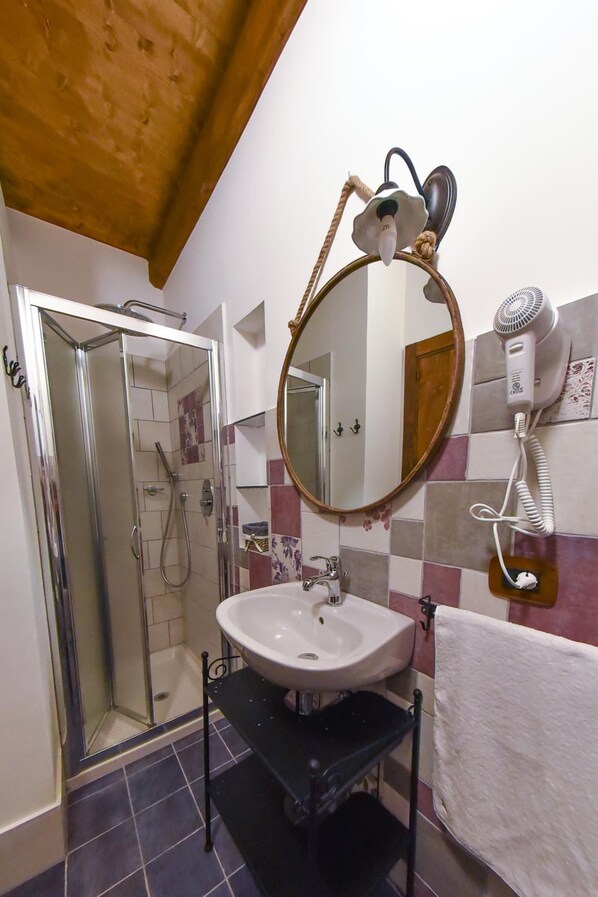 A bathroom with a shower, a sink, a mirror, and a hairdryer mounted on the wall. - B&B Parco Dei Templi (Agrigento)