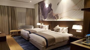 A hotel room with two beds, a desk, a chair, and a large abstract wall art piece.