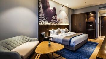 A modern hotel room with a large bed, a sofa, a small round table, and a large abstract painting on the wall.