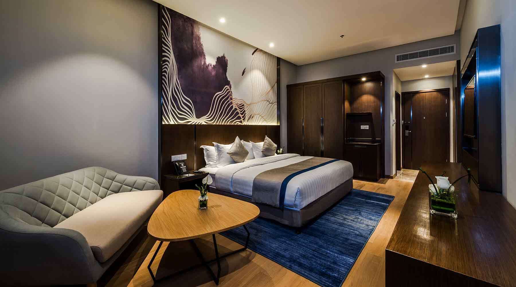 A modern hotel room with a large bed, a sofa, a small table, and a desk.