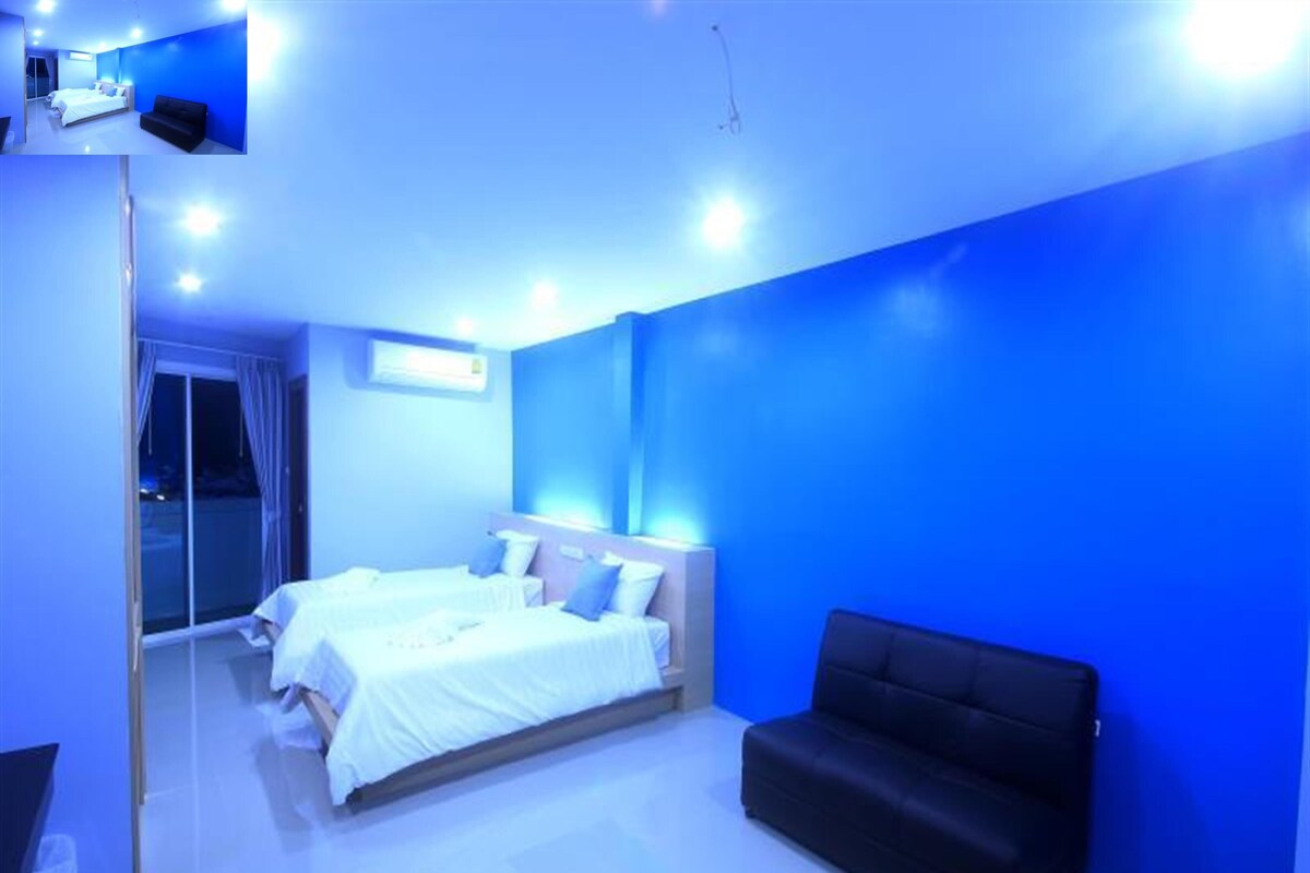 A modern bedroom with two beds, a black sofa, and a large window.