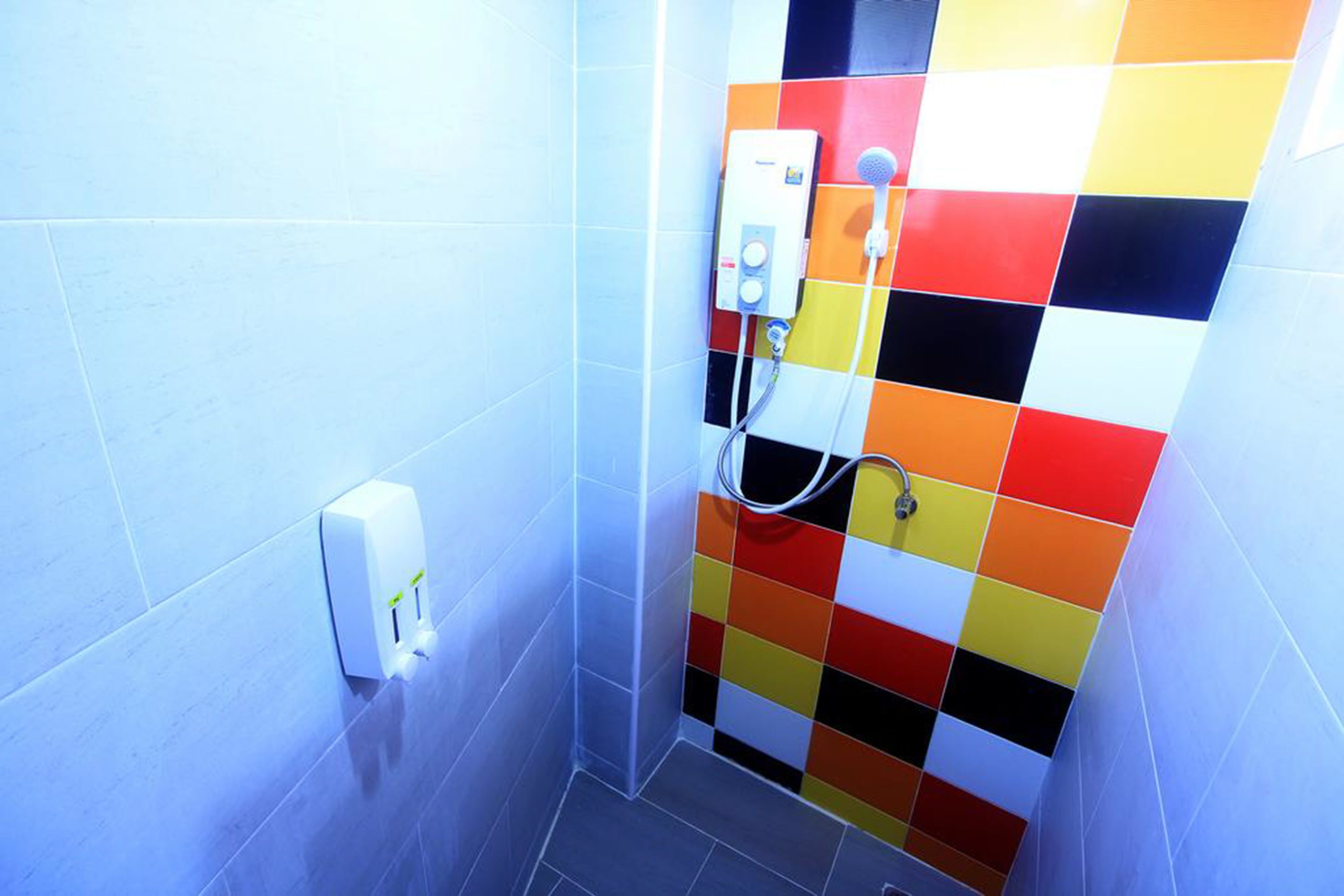 Ein Badezimmer mit Dusche, Seifenspender und farbenfroher Wandfliesen.