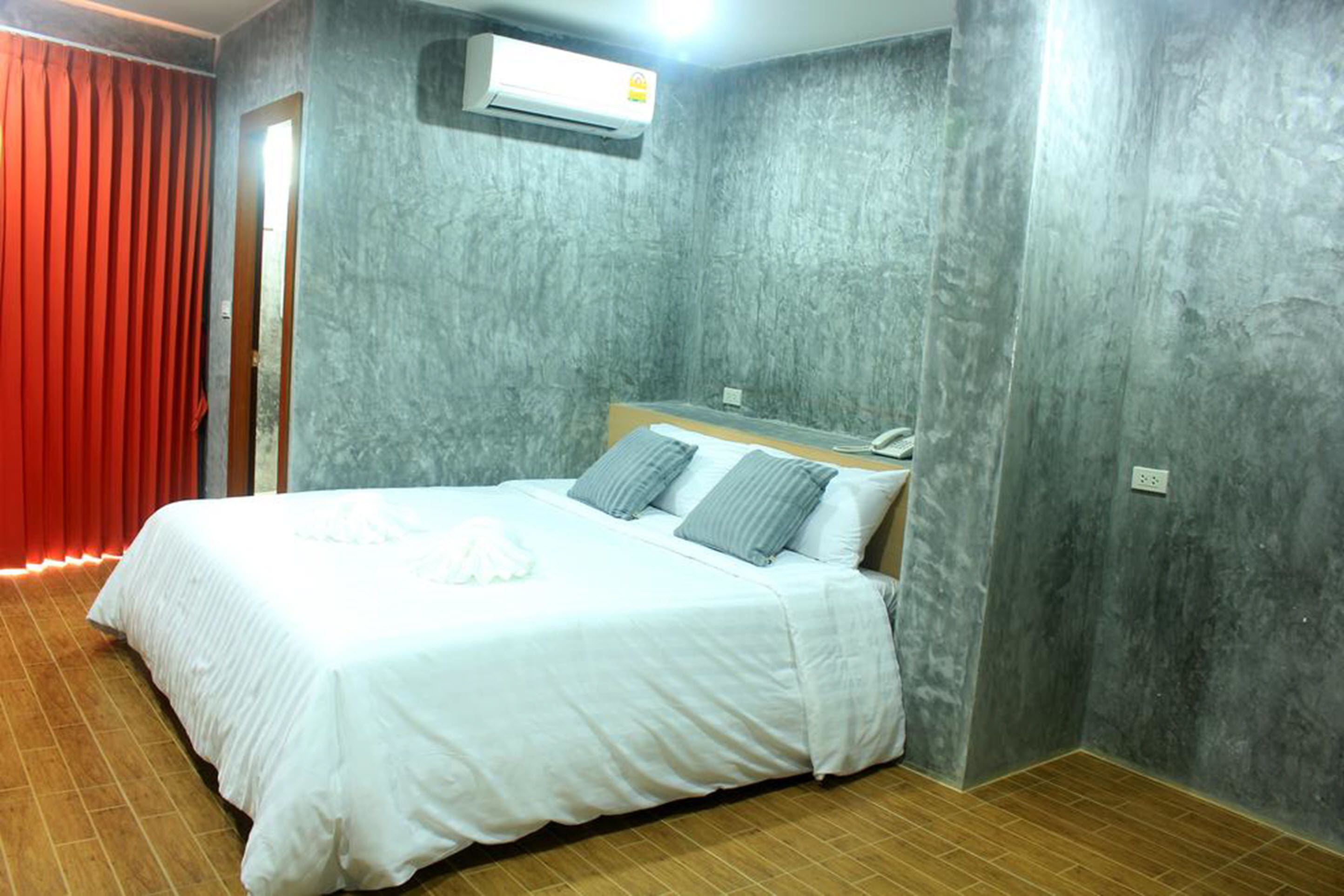 Una habitación con cama, paredes de textura gris, una cortina roja y un equipo de aire acondicionado.