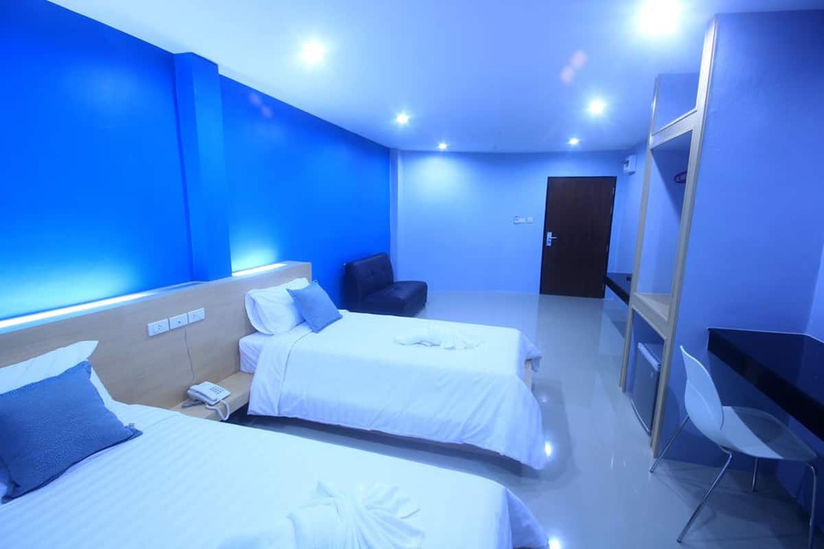 A hotel room with two beds, a desk, a chair, and a door.