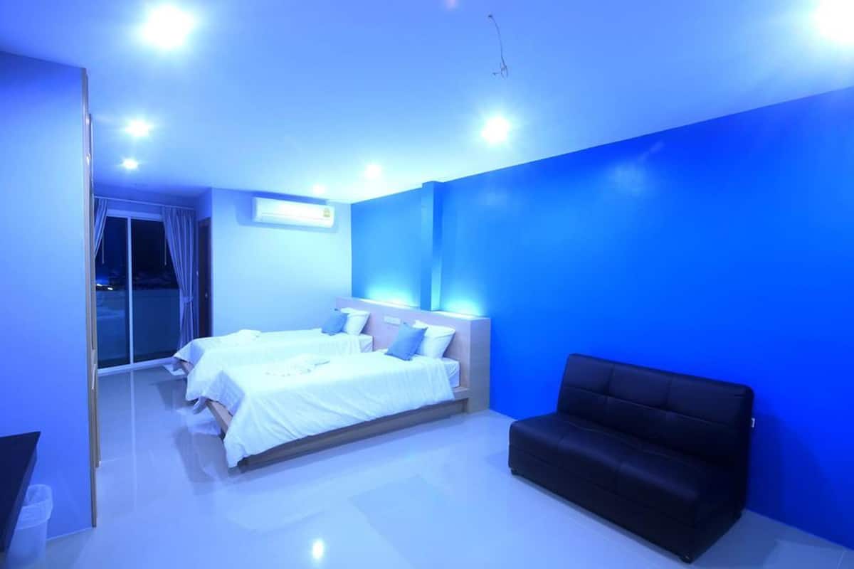 A modern bedroom with a large bed, a black sofa, and a bright blue wall.