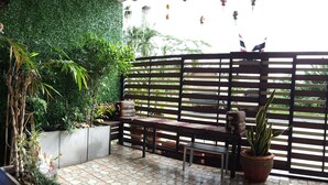 An outdoor seating area with a wooden bench and table, surrounded by potted plants and a green wall. - Sukkasem Guesthouse Thungsong (Thung Song)