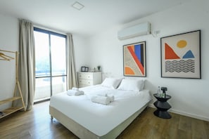 A modern hotel room with a large bed, a side table, a wardrobe, and a window with curtains.