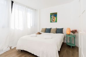 Een slaapkamer met een bed, kussens, een nachtkastje met een lamp en een schilderij aan de muur.