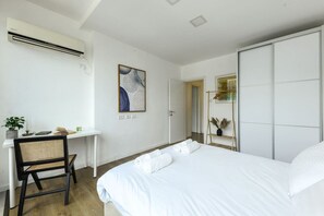 Une chambre d’hôtel avec un lit, un bureau, une chaise, un climatiseur et un tableau au mur.