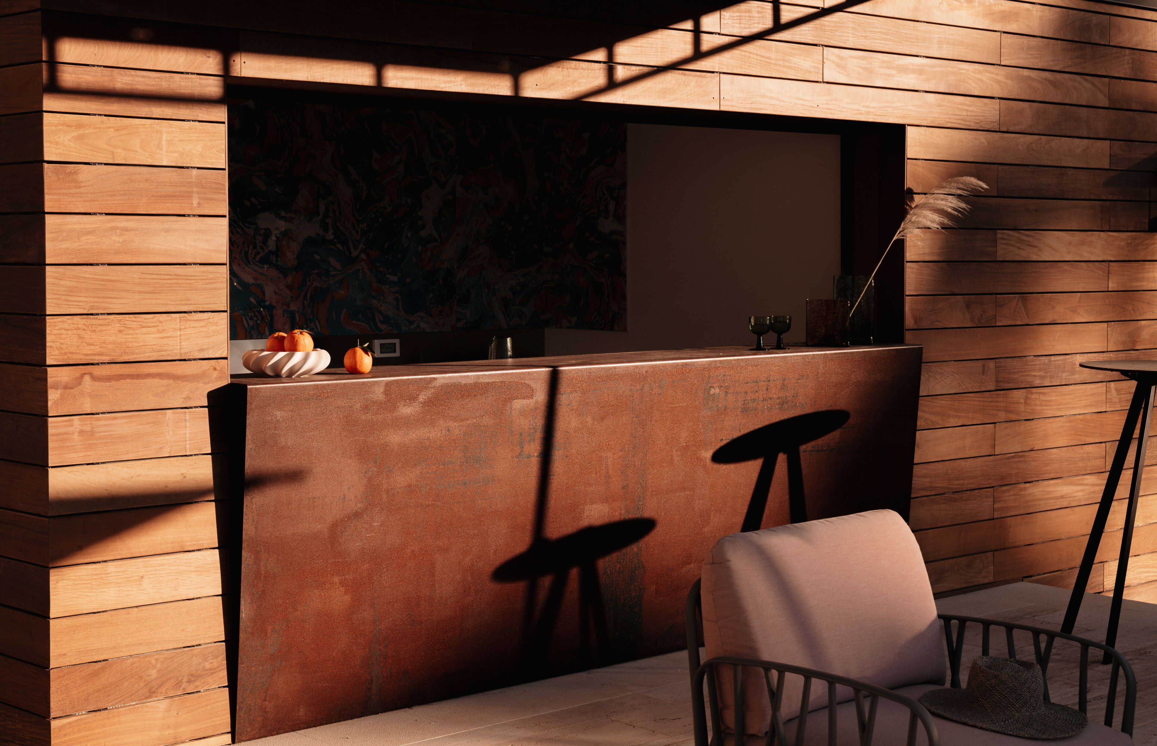 A modern bar area with wooden paneling, a counter, stools, and a chair.