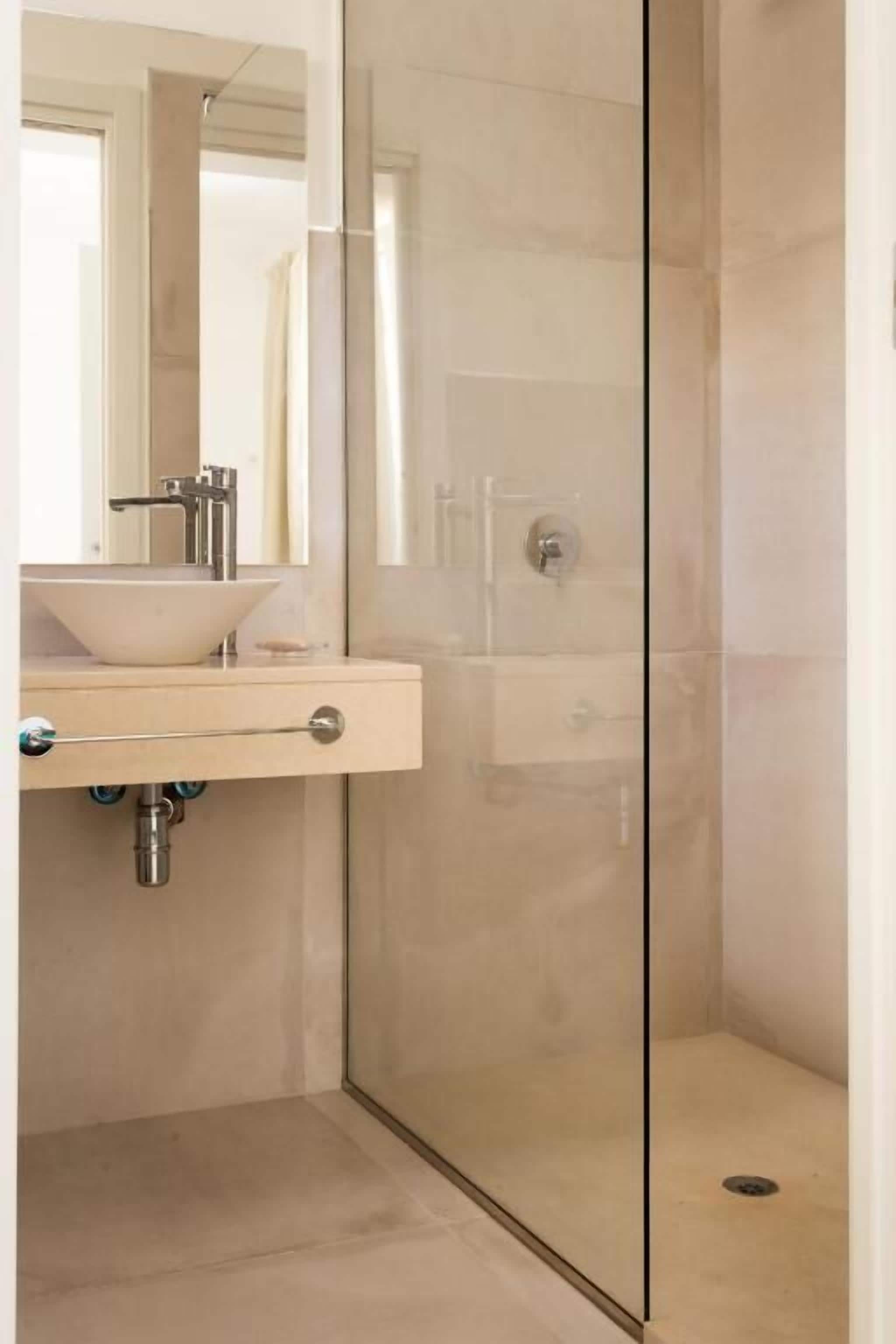 Un baño moderno con ducha de vidrio, tocador color beige con lavamanos y un espejo sobre el tocador.