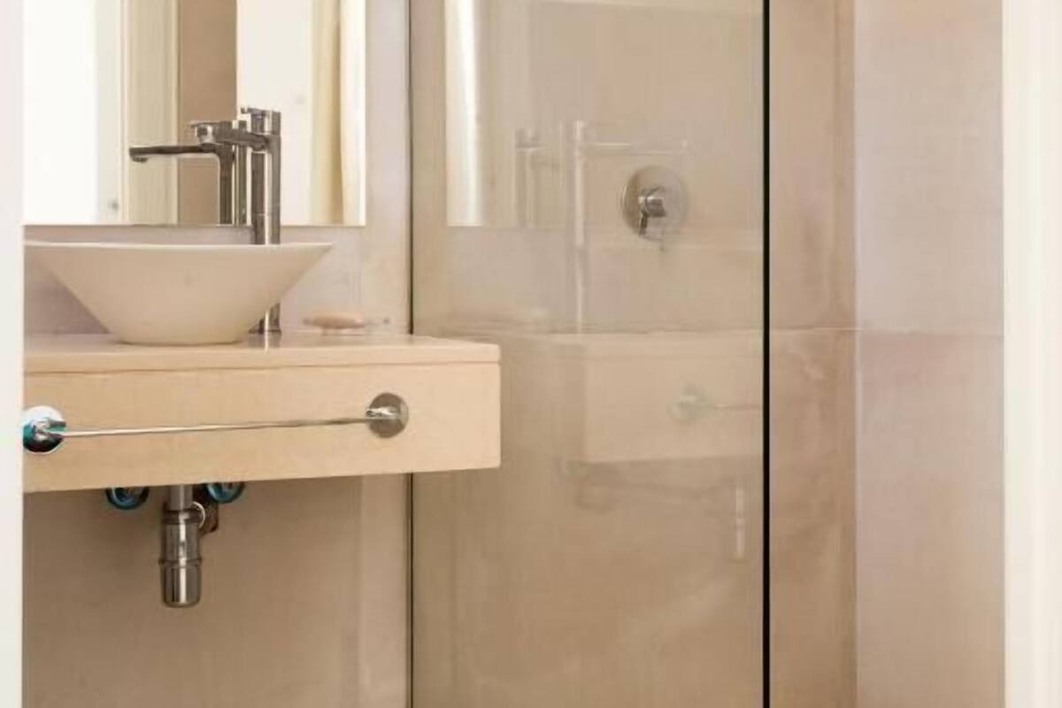 Un baño moderno con ducha de vidrio, tocador color beige con lavamanos y un espejo sobre el tocador.