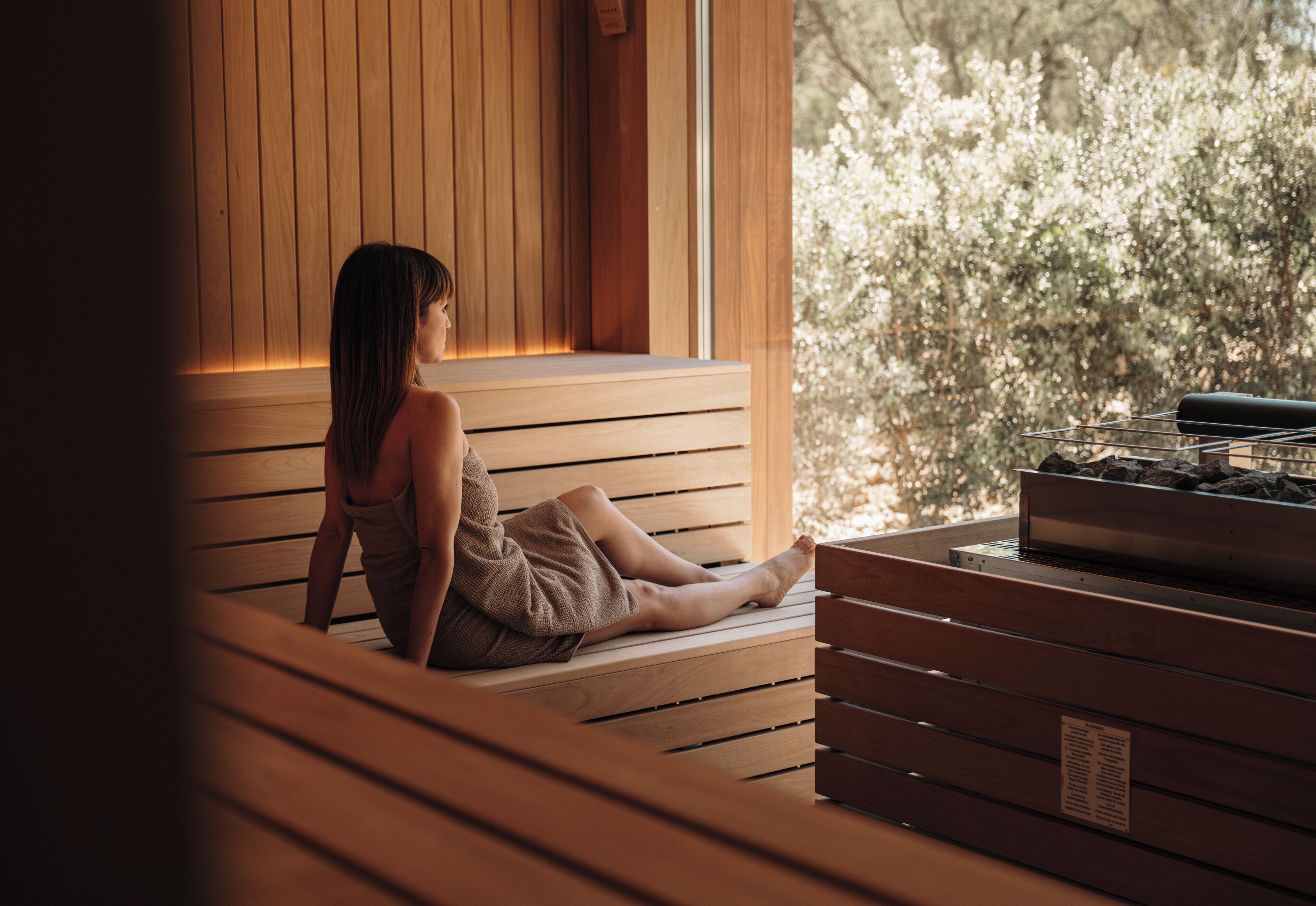 A person sitting on a wooden bench in a room with a window, overlooking a garden.