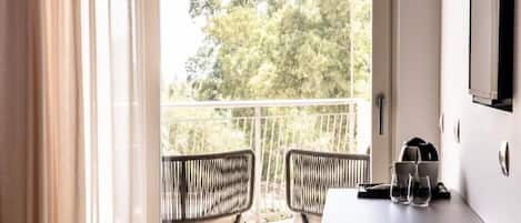 Une chambre avec un balcon, deux fauteuils en osier, une table avec des verres et une bouilloire, et un téléviseur fixé au mur.