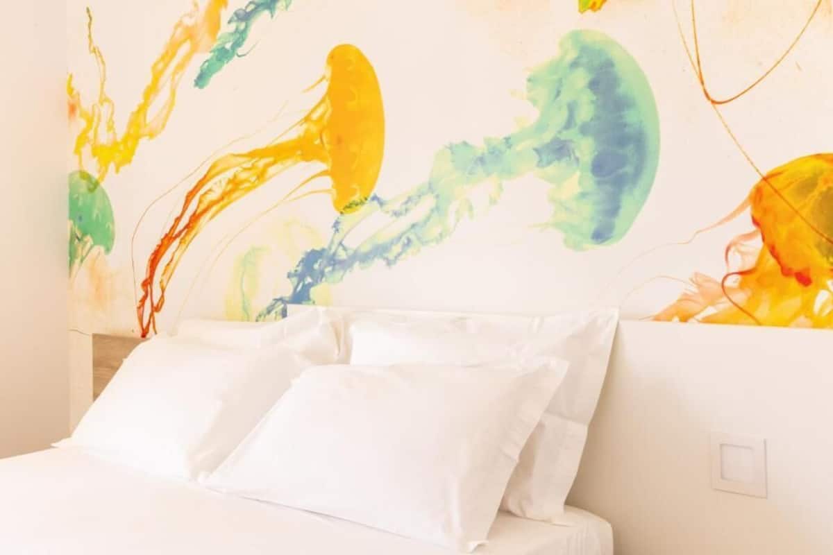 Un lit avec une literie blanche et une peinture abstraite aux couleurs vives accrochée au mur derrière.