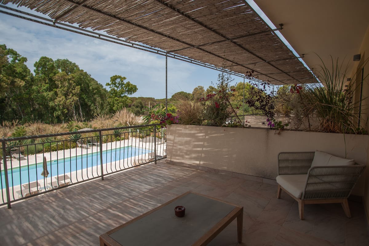 A covered patio with a pool, outdoor furniture, and lush greenery.