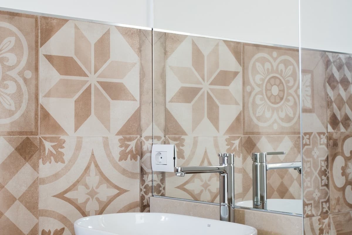 A bathroom with a white sink, a mirror, and patterned tiles on the wall.