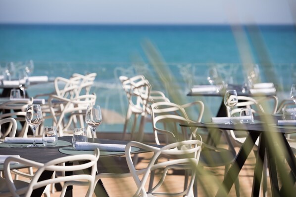 Ein Restaurant mit Tischen und Stühlen, das zum Strand hinaus blickt.