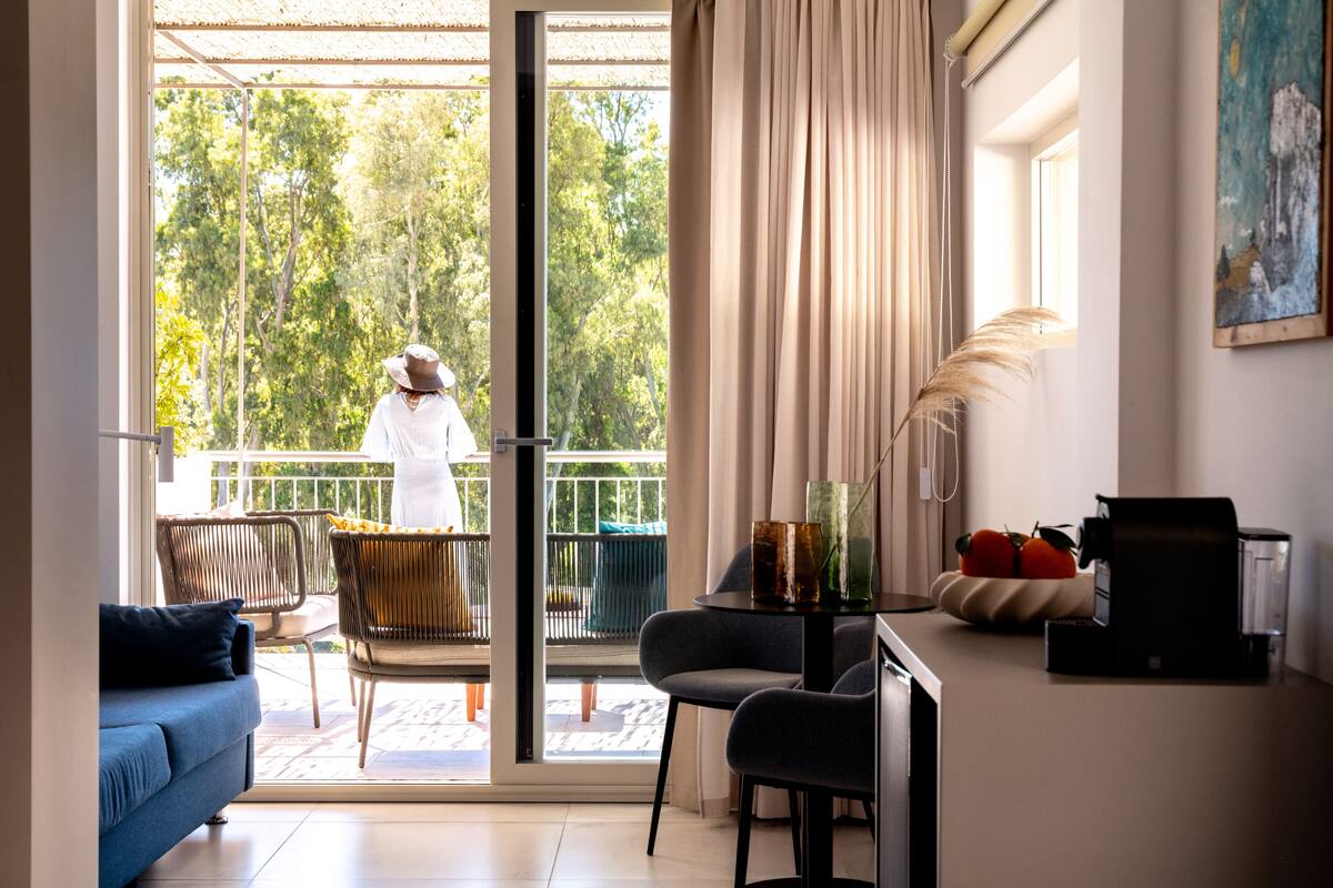 Una sala de estar moderna con un sofá, sillas, una mesa de centro y un balcón con vistas a árboles.