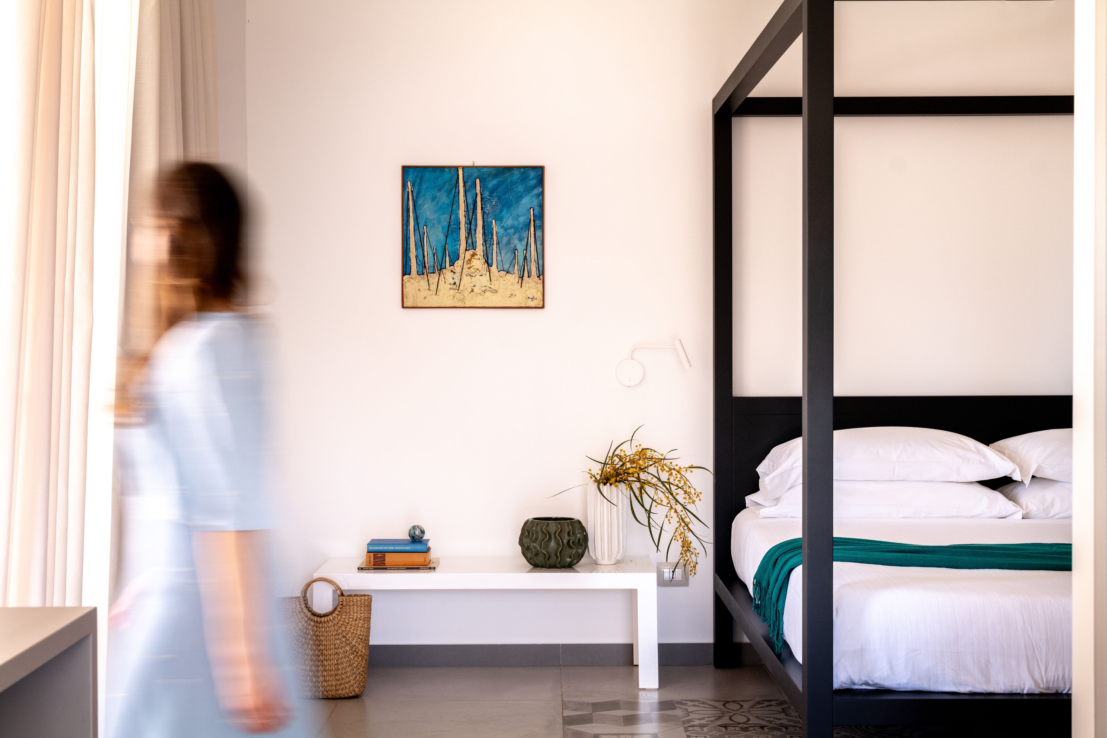 A modern bedroom with a bunk bed, a bedside table with books and a vase, and a painting on the wall.