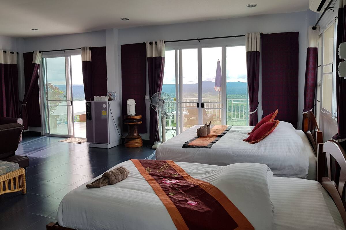 Een hotelkamer met twee bedden, een koelkast, een koffiezetapparaat, een ventilator en uitzicht op de bergen.