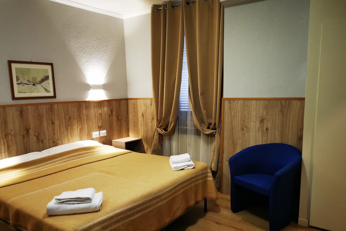 A hotel room with a bed, a chair, a small table, and a window with curtains.