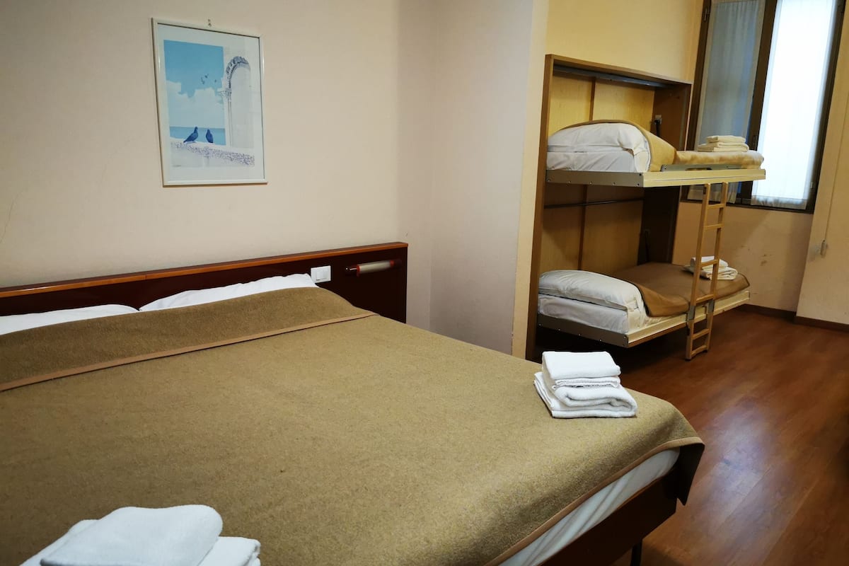 A room with a bunk bed, a single bed, and a poster on the wall.