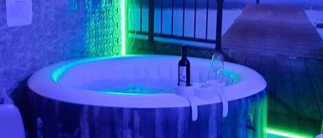 A hot tub with a bottle and glass, surrounded by a blue-lit environment.