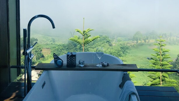 A bathroom with a bathtub, a towel, and a glass of water on a wooden deck overlooking a lush landscape. - The Proud Green Garden Hill Resort (Khao Kho)