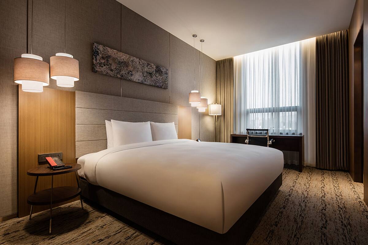 Een hotelkamer met een groot bed, een bureau met een lamp, een schilderij aan de muur en een raam met gordijnen.