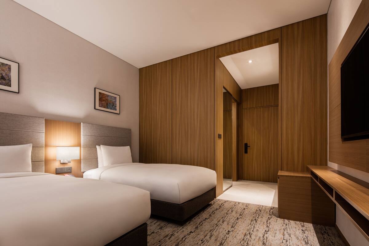 Een hotelkamer met twee bedden, een televisie, een bureau en een houten garderobe.