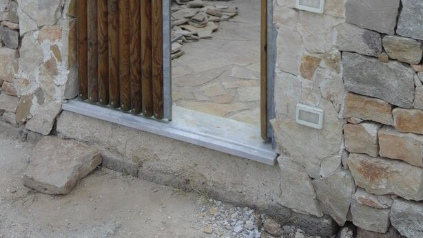 Une arche en pierre surmontée d’un portail en bois, qui mène à une cour intérieure agrémentée d’un arbre et d’un mur en pierre.