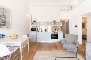 A modern kitchen with white cabinetry, a dining area with a white table and chairs, and a grey armchair. - MAMAD - Jaffa Charm Seaview Stay by Sea N' Rent (Tel Aviv)